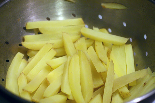 Boiled potato fries drained in a metal colander.