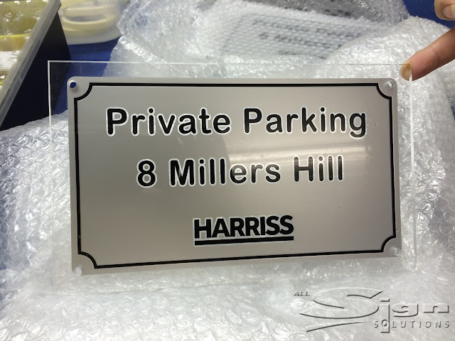 Private Parking 8 Millers Hill Harriss Property information sign on clear perspex with silver vinyl background a black vinyl border shaped for the drill holes that will hold the metal fixings. The black vinyl text has a small clear border between the silver and black giving the sign an extra layered dimension.