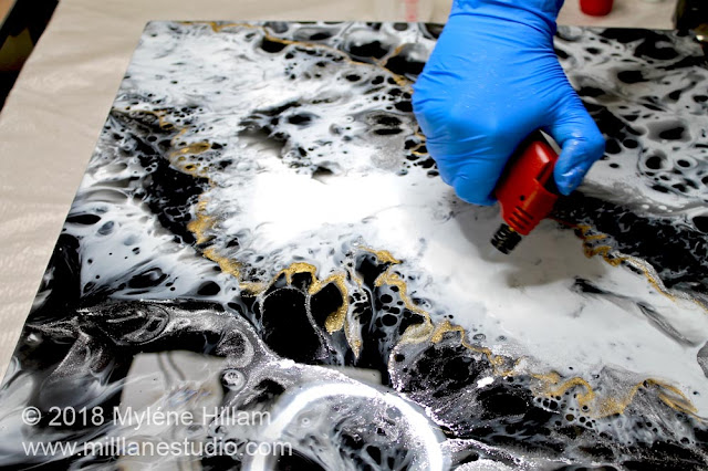 Passing a flame across the surface of the resin canvas to pop any bubbles.