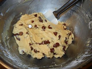 cookie dough in a metal bowl with chocolate chips mixed in with a rubber spatula 
