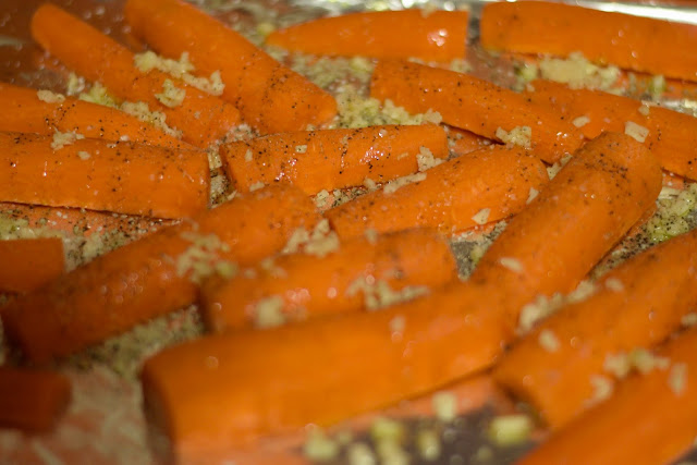 The carrots on the baking sheet, drizzled with oil, sprinkled with garlic, and seasoned with salt and pepper. 