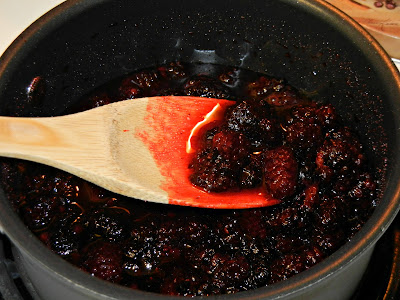 blackberries being cooked in a pot with a wooden spoon 