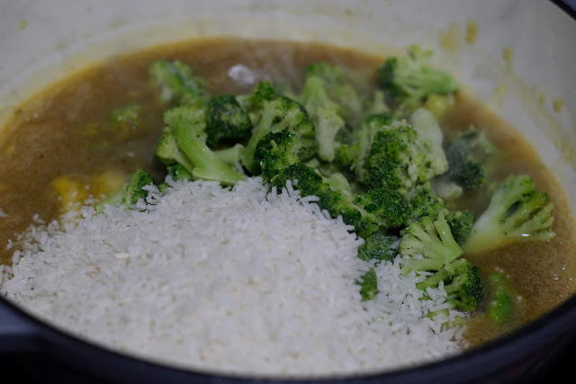 The instant rice and frozen broccoli florets being added to the pan with the broth mixture. 