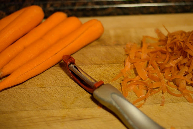 The peeled carrots, a peeler, and the carrot peelings on a cutting board. 