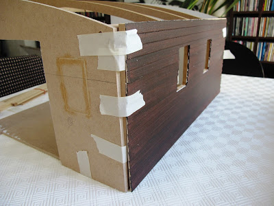 A half-built dolls' house shed, with weatherboard cladding masking taped onto the rear wall.