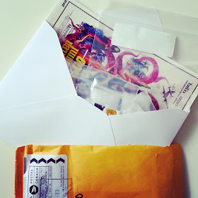 Opened bubble bag with an envelope sticking out of it. Inside the envelope is a Bollywood film poster card, and a number of small zip-lock bags.
