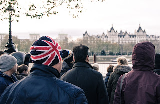 Stock photo taken from behind a crowd of people facing the Thames in London. A man in the foreground is wearing a knit cap patterned after the Union Jack.