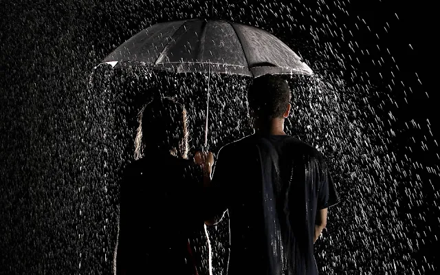 Jongen en meisje in de regen met paraplu in het donker