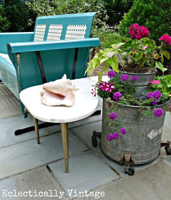 This vintage tin planter, bright blue bench, and marble side table give this porch decor a very eclectic theme