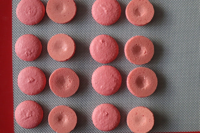 Macaron shells with one pair indented lying on a silicon mat.