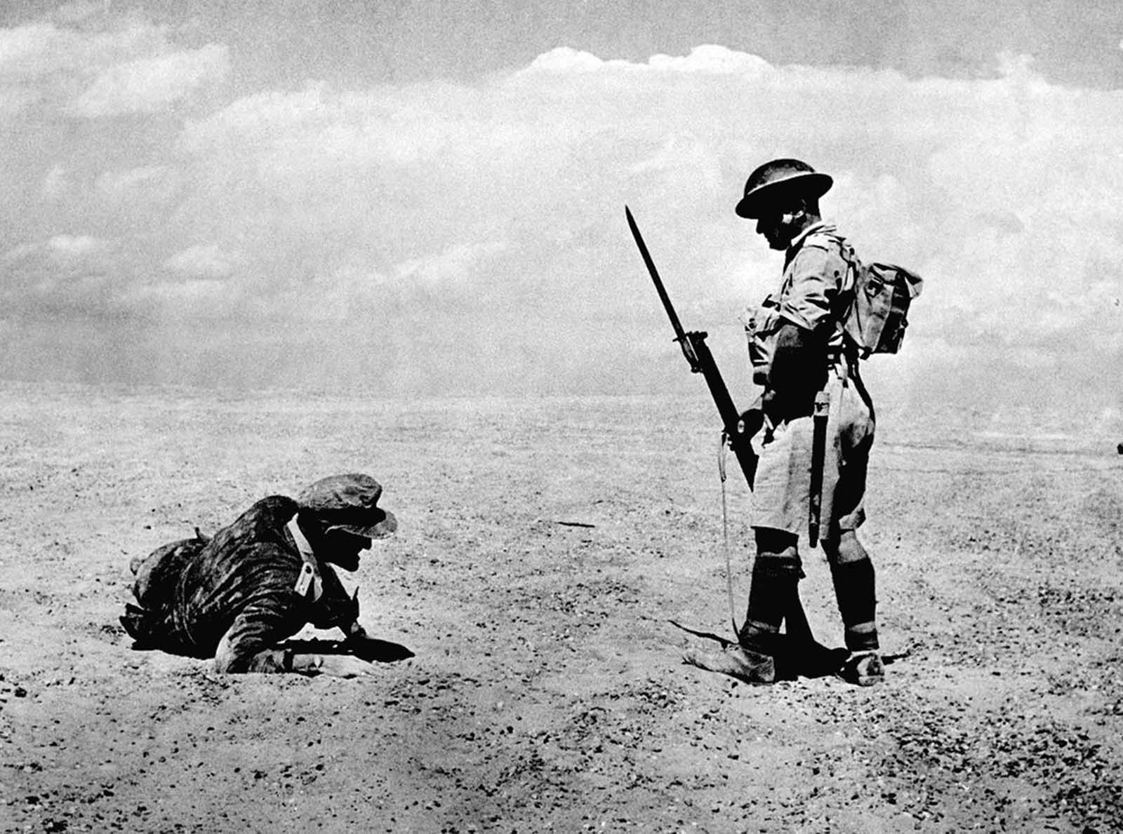 A wounded German officer, found in the Egyptian desert during the first two days of a British offensive, is guarded by a sentry while awaiting backup, on November 13, 1942. 