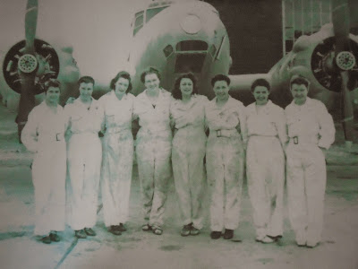 Eight female mechanics standing in front of a WWII airplane