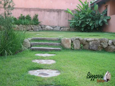 Detalhe da construção do muro de pedra com pedras grandes sem cimento com os caminhos de pedra bruta, a escada de dormente de madeira e a execução do paisagismo em sítio em Mairiporã-SP.