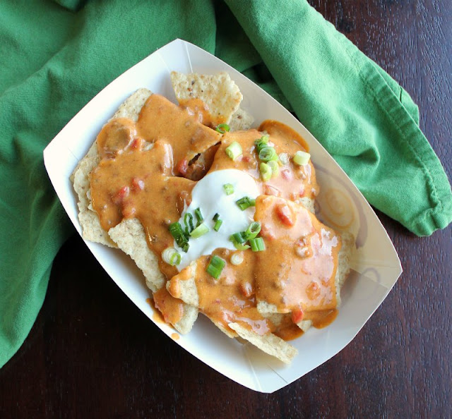 Queso is the ultimate party food and is a must for tailgating and watching the game at home. This tailgate queso is full of flavor and it is super simple to make. dish of nachos topped with tailgate queso, sour cream and green onions