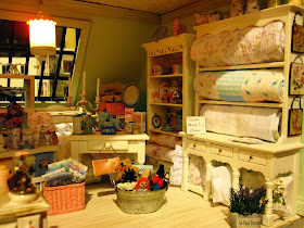 Modern miniature shabby chic shop display of linens and quilts on cream shelves.