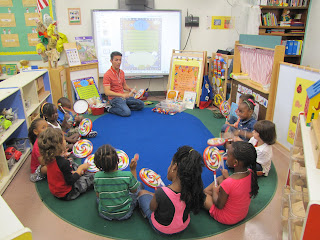 Alex dá aula para as crianças sentadas no chão.  Foto de Carla Guarilha.