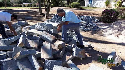 Bizzarri escolhendo as pedras folhetas de granito na cor azul claro sendo essa pedra cortada a mão para fazer as guias de pedra na rua de pedra com o piso de pedrisco.