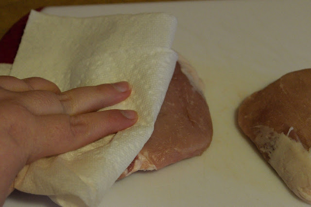 Patting the pork chops dry with a paper towel.