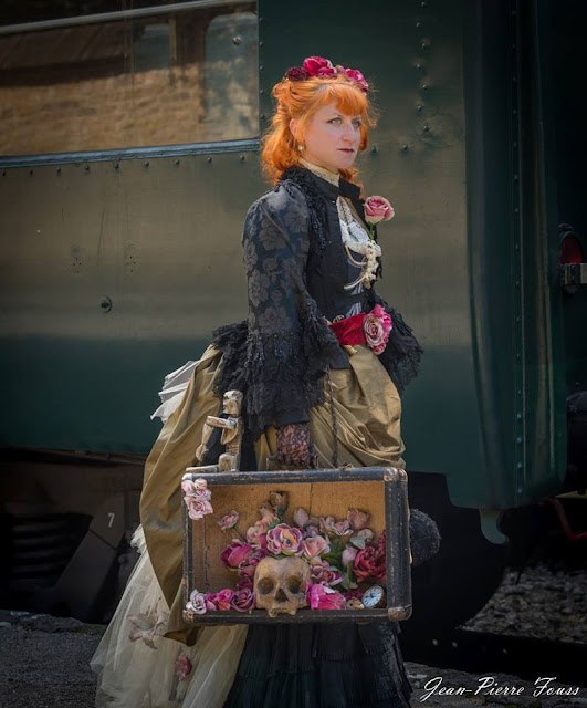 Woman dressed in gothic victorian steampunk clothing with a suitcase filled with roses, flower petals, skull and skeleton. women's steampunk clothing and costumes