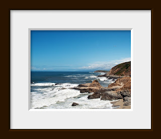A photo of the Pacific ocean's waves crashing into the rocky coastline with a beautiful sunny blue California sky and dramatic distant rain clouds in the background.
