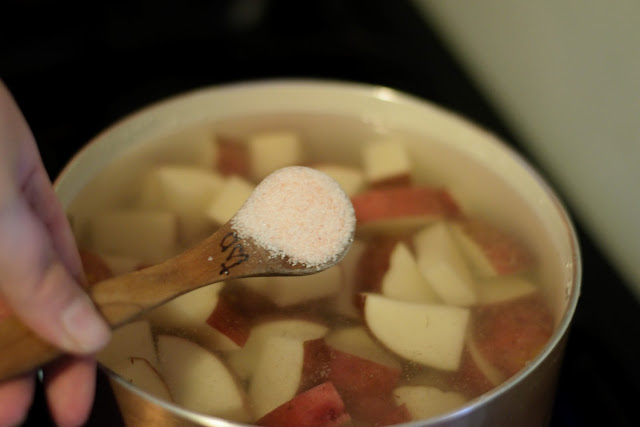 A teaspoon of salt being added to the pot of potatoes and water. 