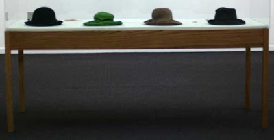 Raised glass case with four women's hats in it, one is bright green, the others dull colors