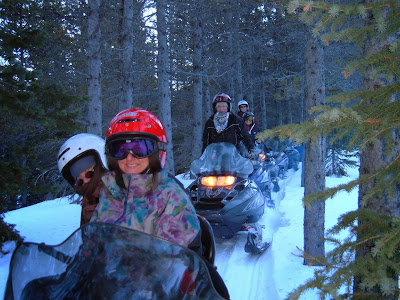 Snowmobile tour with five guests, riding on a trail through the trees.