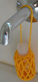 The orange mesh shower gel drawstring bag is hanging on the bath spout with a small bottle of shower gel inside.