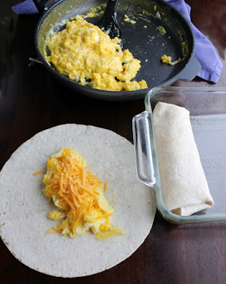 pan of scrambled eggs with some eggs and cheese on a tortilla ready to be rolled into burrito