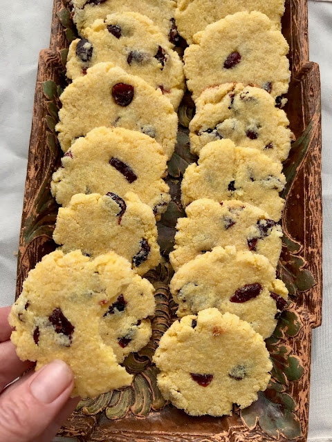 Hand holding a cranberry cornmeal cookie with a bite out of it.