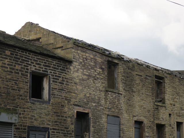Empty buildings with missing and blocked up windows, plastic and plants on slate roof