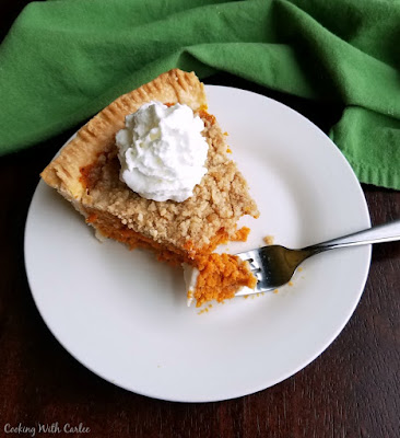 This carrot pie is topped with a buttery cinnamon streusel. It is a fabulous combination that will make you wonder where carrot pie has been your whole life! It's perfect for Easter, Thanksgiving or just because! piece of carrot pie topped with whipped cream, first bite on fork