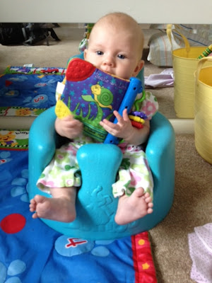 Photo of baby sitting in a blue seat and holding a multi-colored 'cloth book.'