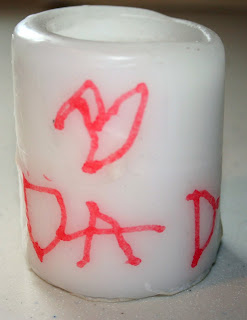 A finished candle that says "dad" on a white candle 