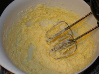 eggs, butter, and sugar being creamed together in a white bowl with a hand mixer 