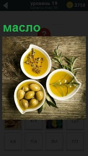 На столе находятся три блюда с маслом и оливками внутри , рядом положены зеленые ветки