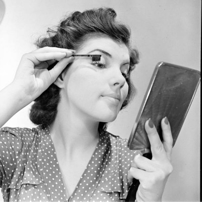 Nina Leen photo of young lady applying mascara in front of mirror wearing polka dot dress