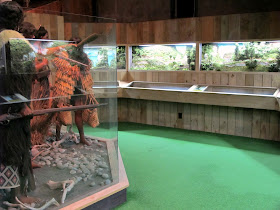 Room with full-scale models of Maori in traditional dress on the left, and a long diorama on the right.