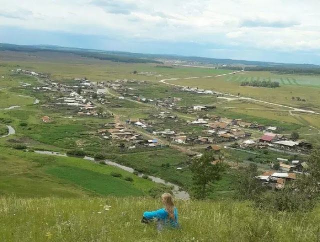 Chica rusa en aldea. Sentada en colina.