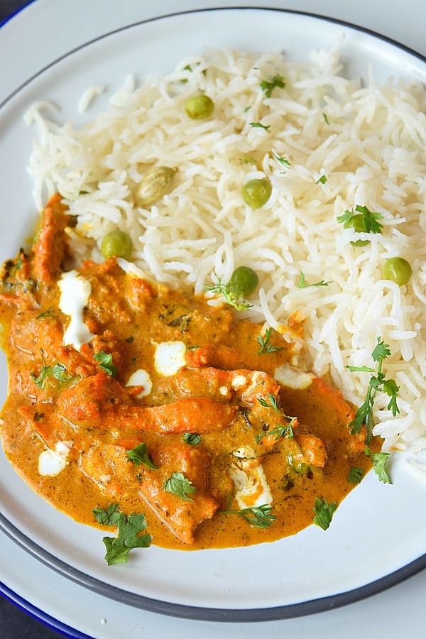 Delicious creamy Butter Chicken served in a white plate with plain peas pulao