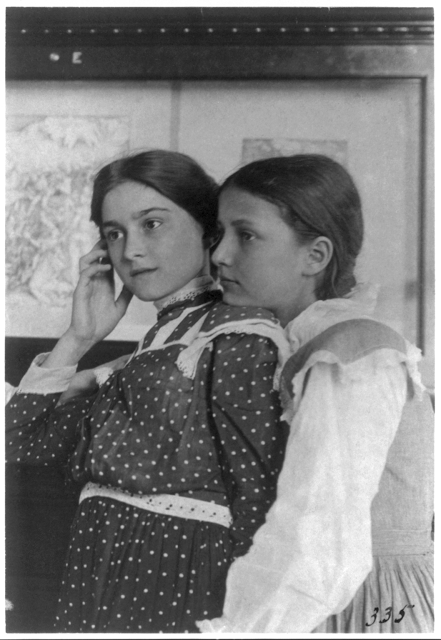 Two girls from a Washington, D.C., school on a class visit to the Library of Congress, looking at an exhibit of relief or wood engravings, one with her chin on shoulder of the other, 1899.