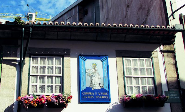 Duas janelas com floreiras e um paine de azulejo escrito: compra e venda de livros usados