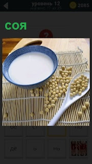 На рогожке стоит тарелка с молоком и семена соя, из которых готовят продукты питания