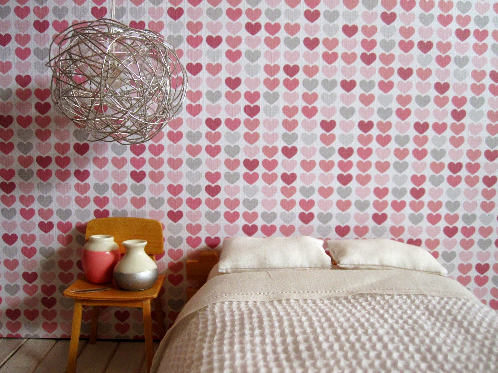 Modern dolls' house miniature bedroom scene with futon bed with a white waffle-weave blanket, a blonde-wood chair holding two dip-painted white vases and a large round wire lightshade.