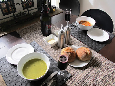 Two bowls od soup (both different), two rolls, and two glasses of sparking shiraz on a dining table.