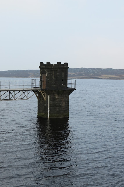 A stone pump tower rising from the water with a steel walkway connecting it to dry land.