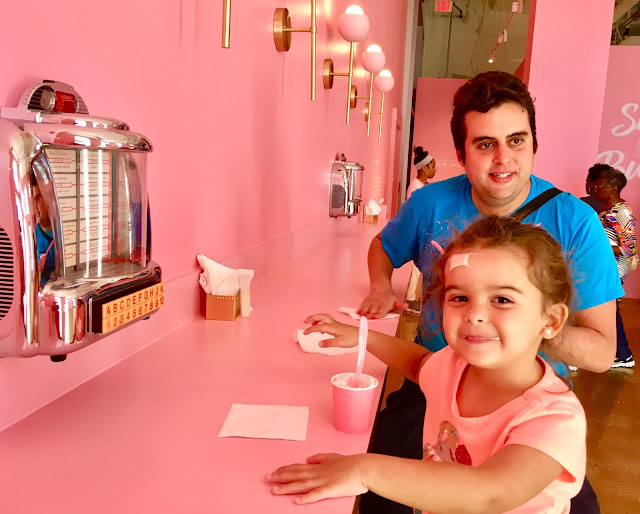 Toddler and her dad enjoy small milkshakes in front of a small jukebox