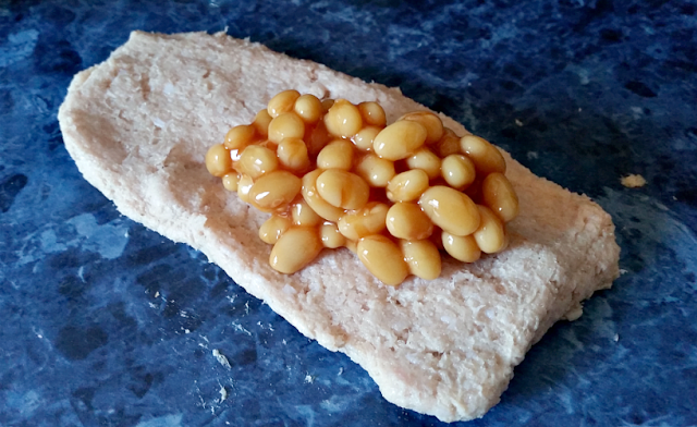 a square of sausage meat with baked beans on top