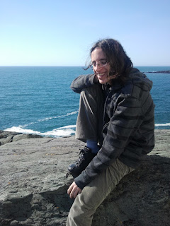 Photo of a young man sitting on a large rock in front of the ocean