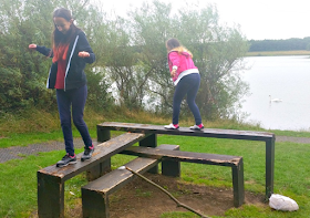 My two girls climbing and balancing on planks of wood next to a lake
